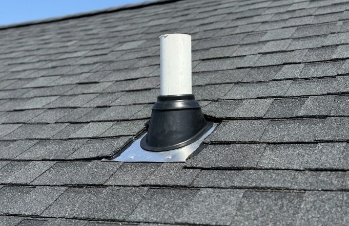 New black rubber pipe boot with a metal flashing base installed around a white plumbing vent pipe on a dark gray asphalt shingle roof.